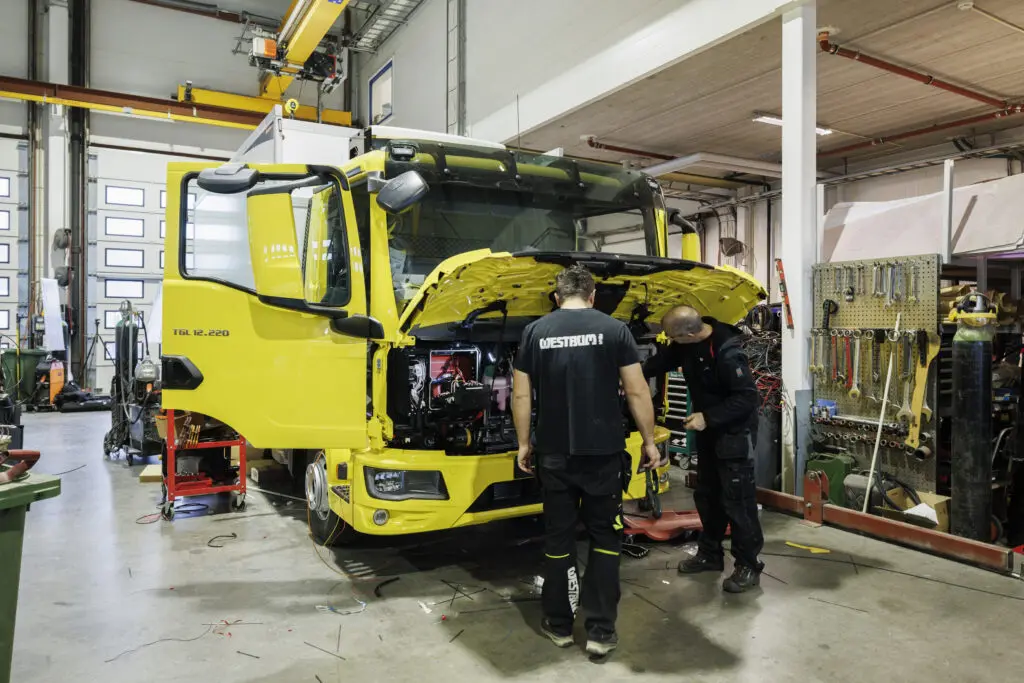 bildet viser toansatte hos westrum som ser i motorrommet på en gul lastebil